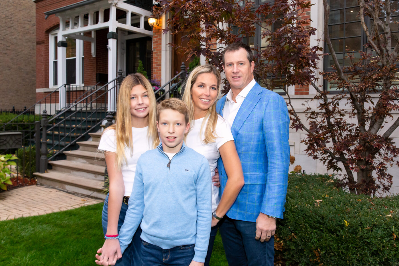 family girl in white shirt, brother in blue shirt mother in white shirt dad in blue blazer posing in front of house in Lincoln park chicago